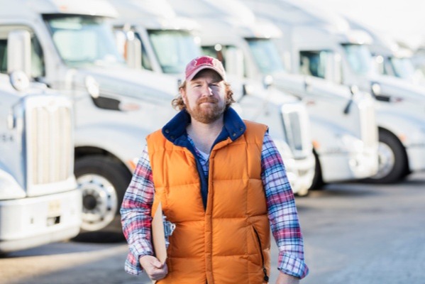 Truck driver standing in front of a large fleet that combined during the Worldwide Express and GlobalTranz merger